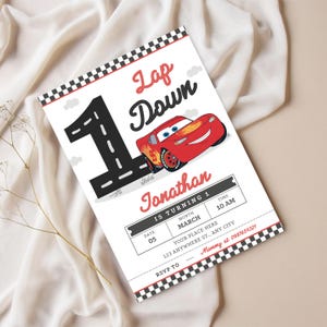Könnte beinhalten: Eine weiße Einladungskarte mit einem rot-schwarz karierten Rand. Die Karte zeigt ein Cartoon-Bild eines roten Rennwagens und den Text "Lap Down". Die Karte ist für Jonathans ersten Geburtstag, mit Datum, Uhrzeit und Ortsangaben.