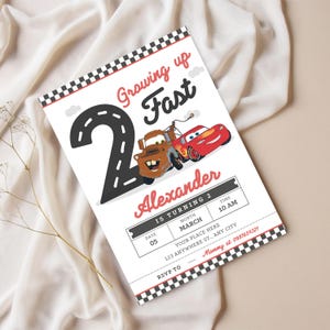 May include: A white invitation card with a black and red chequered border. The card features a large number 2 in black, a road design, and cartoon cars. Text includes "Growing up Fast" and "Alexander is turning 2".
