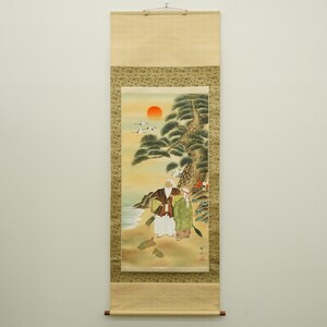 以下が含まれることがあります： 海岸にいる2人の人物を描いた日本の巻物絵画。赤い太陽が崖の上に沈む様子が描かれています。この作品は、緑、茶色、黄色を基調とした、細部までこだわった筆遣いが特徴です。巻物は装飾的な縁で縁取られています。