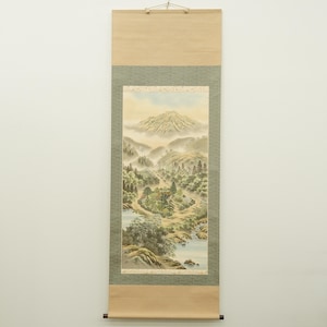 Könnte beinhalten: Vertikale Rollbildmalerei, die eine Berglandschaft mit einem Fluss und Bäumen zeigt. Das Kunstwerk zeigt einen Berggipfel im Hintergrund, mit einem Fluss und Bäumen im Vordergrund. Die Rolle ist in Grün und Beige gerahmt.