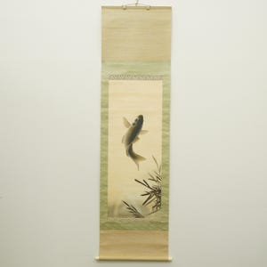 May include: A vertical scroll painting depicting a carp in grey and black, with bamboo details. The artwork has a light green border and a beige background, creating a serene and traditional aesthetic.