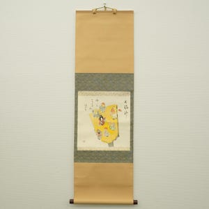 以下が含まれることがあります： 黄色い背景に人物のカラフルなイラストが描かれた、伝統的な日本の巻物絵。巻物は紙と木でできており、上部に吊り下げ用のループが付いています。