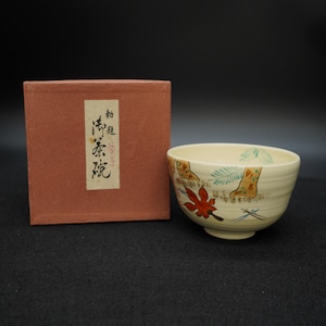 以下が含まれることがあります： クリーム色のセラミックティーボウル。赤いカエデの葉と様式化された木のハンドペイントデザイン。ボウルには、日本語のテキストが入った赤褐色の箱が付属しています。ボウルはテクスチャ加工された表面を持っています。
