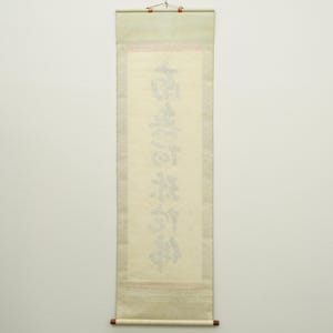 May include: A traditional Japanese scroll with calligraphy in black ink. The scroll features a light beige background with a green top and a brown bottom rod. The calligraphy is vertically oriented and centered on the scroll.