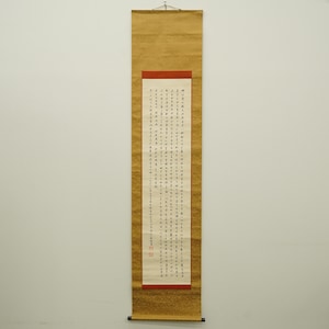 Peut inclure: Un rouleau vertical avec calligraphie noire sur papier crème. Le rouleau est encadré d'une bordure dorée et présente un accent rouge en haut de la calligraphie. Une baguette noire est en bas.