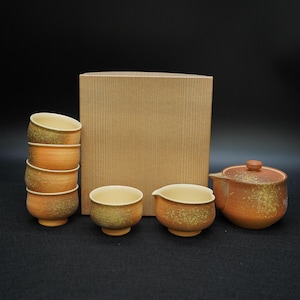 May include: A Japanese tea set with a stack of six small tea cups, two individual cups, a small pitcher, and a teapot with a lid. The tea set is a speckled orange and yellow color, and is next to a brown box.