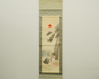 May include: A traditional Japanese hanging scroll painting. The artwork depicts a coastal scene with figures, a tree, and a setting sun. The scroll is framed with a green border and has a hanging mechanism at the top.