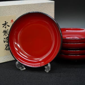 以下が含まれることがあります： 黒い縁取りの赤い漆器のボウルセット。 ボウルは積み重ねられており、透明なスタンドに1つのボウルが置かれています。 ボウルは光沢のある仕上げで、セットの一部である可能性があります。