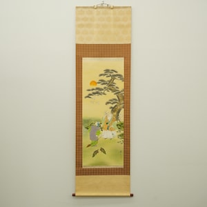 以下が含まれることがあります： 風景画が描かれた日本の掛け軸。夕日と木々のそばにいる人物が描かれています。柔らかい色使いで、装飾的な縁と下部に木製の棒が付いています。