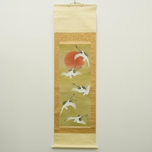 May include: A Japanese scroll painting depicting a red sun and six white cranes in flight. The cranes have black markings on their wings and heads. The scroll has a cream-coloured top and bottom with a gold patterned border.