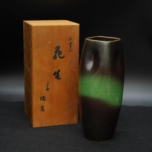 以下が含まれることがあります： 黒と緑の花瓶と木箱。花瓶は黒から緑に変わるグラデーションカラーです。木箱には日本語の文字が書かれています。