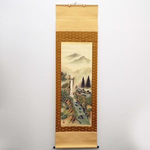 Puede incluir: Pintura en rollo vertical que representa un paisaje montañoso brumoso con una cascada, árboles y pequeñas casas. La obra de arte está enmarcada por un borde estampado y tiene un mecanismo para colgar de madera.