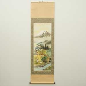 Peut inclure: Un rouleau mural vertical présentant une peinture d'un sommet enneigé au-dessus d'un paysage avec des pins, une petite maison, du bambou et deux oiseaux blancs près d'un ruisseau. Le rouleau a une bordure beige et un cadre en tissu vert olive.