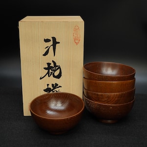 Pode incluir: Um conjunto de seis tigelas de madeira com acabamento natural, exibidas com uma caixa a condizer. As tigelas são empilhadas e dispostas ao lado da caixa, que tem caracteres japoneses.