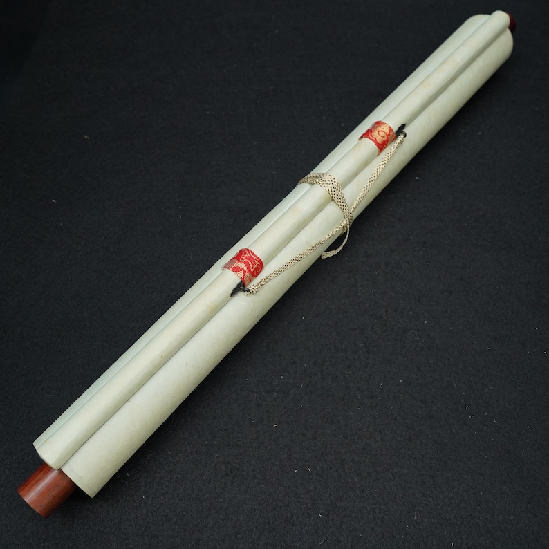 May include: A rolled-up scroll with a cream-colored paper and wooden dowels. The scroll is secured with a gold chain and sealed with red wax stamps. The background is a solid black.