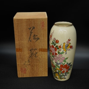 May include: Cream-colored ceramic vase with a gold rim, featuring a floral and bird design in red, pink, yellow, and green. The vase is next to a wooden box with Japanese characters.