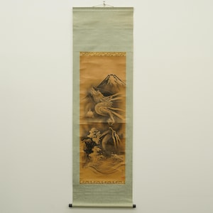 Puede incluir: Pintura tradicional japonesa en rollo que representa un dragón y el monte Fuji. La obra de arte es principalmente en tonos marrones y negros, con un borde verde claro. El dragón está detallado, con la montaña al fondo.