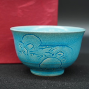 May include: A turquoise ceramic bowl featuring a crackled glaze finish and an embossed design of two small rodents on the exterior surface. The bowl has a rounded shape with a flared rim and a small circular base, showcasing a vibrant blue color.