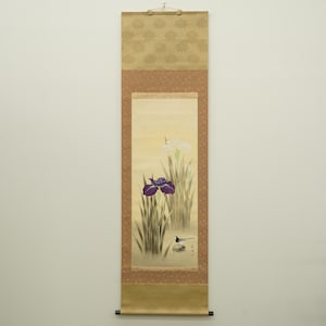 Può includere: Dipinto giapponese verticale su rotolo con iris e un uccello. L'opera presenta un'iride viola e un'iride bianca in mezzo a un fogliame verde. La pergamena ha uno sfondo beige con bordi decorativi e un meccanismo di sospensione in legno.