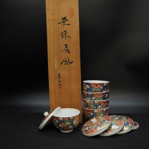 May include: A set of Japanese tea cups and lids with a wooden box. The cups and lids feature a blue, orange, and green floral pattern. The wooden box has Japanese characters.