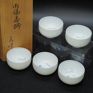 May include: Set of five white ceramic tea cups with a blue wave design inside. The cups are displayed on a clear acrylic stand. A wooden box with Japanese characters is visible in the background.