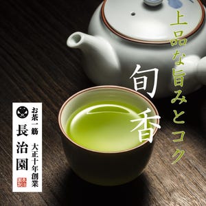Op de afbeelding: Een keramische theekop gevuld met levendige groene thee, naast een witte theepot met een blauw bloemmotief. Japanse tekst is zichtbaar. De theekop is bruin aan de buitenkant en groen aan de binnenkant. De achtergrond is een donker houten oppervlak.