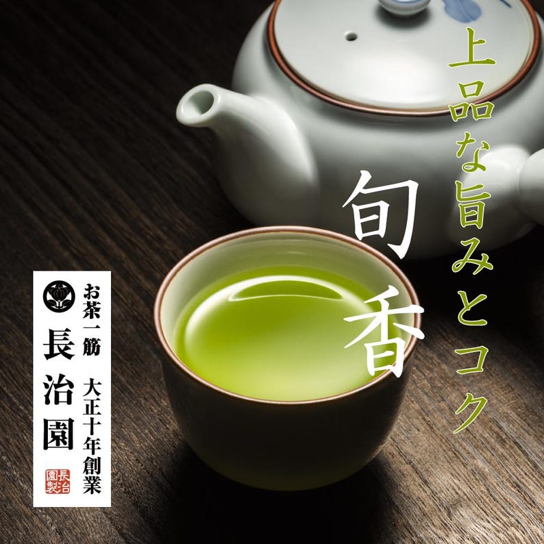 Op de afbeelding: Een keramische theekop gevuld met levendige groene thee, naast een witte theepot met een blauw bloemmotief. Japanse tekst is zichtbaar. De theekop is bruin aan de buitenkant en groen aan de binnenkant. De achtergrond is een donker houten oppervlak.