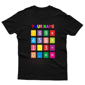 May include: Black t-shirt with a colorful calculator design. The design includes the text "YOUR NAME" above a grid of number and math symbols. The numbers and symbols are in various bright colors.