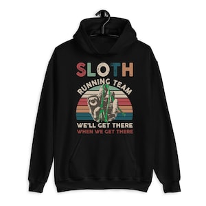 May include: Black hooded sweatshirt with a graphic that reads "SLOTH RUNNING TEAM" above an illustration of a sloth. The design includes a colorful sunset and the text "WE'LL GET THERE WHEN WE GET THERE."
