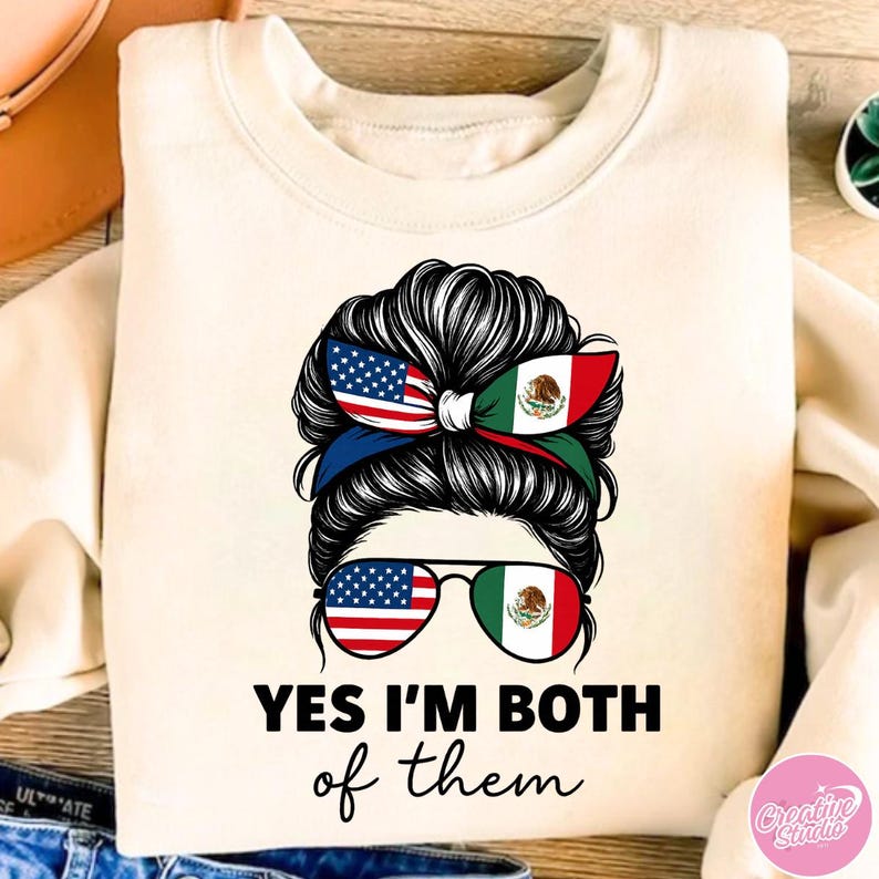 May include: Cream-colored sweatshirt with a graphic of a woman's hair styled with the American and Mexican flags. The sunglasses also feature the flags. The text reads "YES I'M BOTH of them."