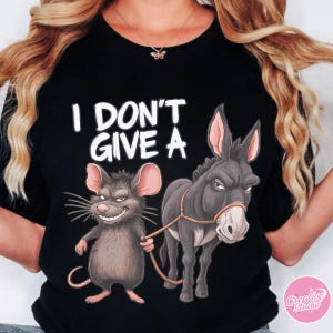 May include: Black t-shirt with the phrase "I DON'T GIVE A" in white block letters. The graphic features a cartoon mouse holding a rope attached to a donkey. The mouse is smiling, and the donkey has a stern expression.