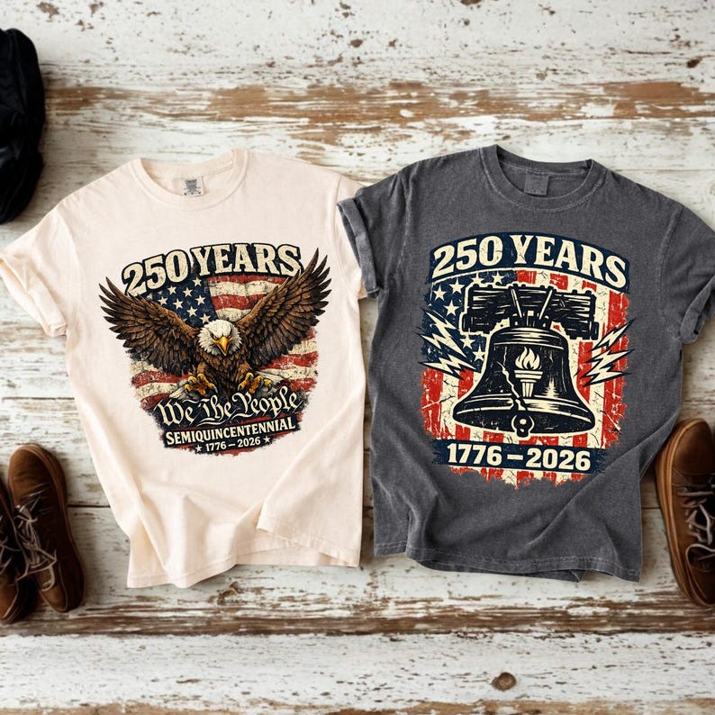 May include: Two t-shirts with patriotic designs. One is cream-coloured with an eagle graphic and the text "250 YEARS" and "We the People". The other is grey with a Liberty Bell graphic and the text "250 YEARS".