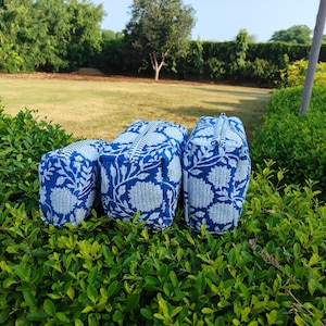 Puede incluir: Tres neceseres con estampado floral azul y blanco con cierres de cremallera. Las bolsas son rectangulares y se asientan sobre un lecho de follaje verde. Las bolsas tienen un patrón floral a juego.