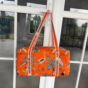 May include: An orange tote bag featuring a tropical bird and palm tree design. The bag has two long straps with a white and red striped pattern. The rectangular bag is made of a textured fabric.