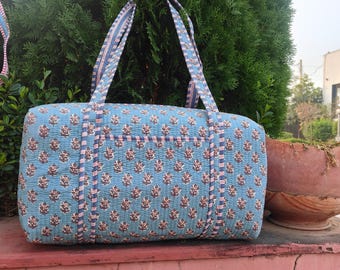 Pode incluir: Uma mala tote acolchoada azul com um padrão floral em castanho e branco. A mala tem duas alças e um bolso na frente. A mala tem aproximadamente 46 cm de comprimento.