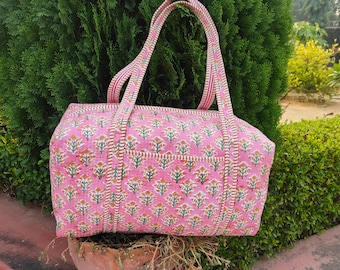 Pode incluir: Bolsa tote rosa com estampa floral e alças combinando. A bolsa apresenta um padrão repetido de motivos florais laranja e verde em um fundo rosa. As alças são listradas em rosa e branco.