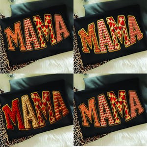 May include: Four black t-shirts with the word "MAMA" embroidered in different styles. The letters are in various colors and patterns, including hearts, zigzags, and knit textures. The shirts are displayed on a white fur-like surface.