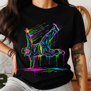 Könnte beinhalten: Schwarzes T-Shirt mit einer Neon-Illustration eines Breakdancers in Bewegung. Das Design verwendet leuchtende Farben wie Pink, Gelb, Grün und Blau mit einem tropfenden Farbeffekt. Eine dynamische Darstellung der Streetdance-Kultur.