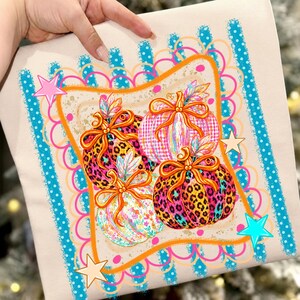 Peut inclure: Un tissu de couleur claire avec une impression graphique de quatre citrouilles ornées de nœuds orange. Les citrouilles présentent des motifs léopard, à carreaux et floraux en rose vif, bleu et jaune. Le design inclut une bordure festonnée.