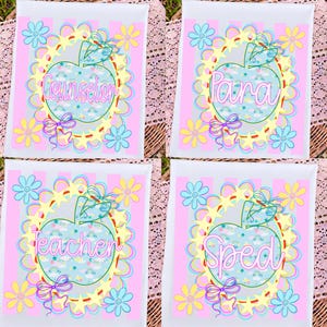 Peut inclure: Quatre panneaux rectangulaires blancs à rayures verticales roses. Chacun présente une pomme centrale avec un motif arc-en-ciel et étoiles bleues, entourée d'une bordure d'étoiles jaunes, de fleurs bleues et de nœuds violets. Texte : Counselor, Para, Teacher, SPED.