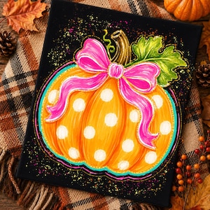 Peut inclure: Une peinture sur toile rectangulaire sur fond noir représentant une citrouille orange vif décorée de pois blancs, un grand nœud rose vif attaché au sommet, une feuille verte et une tige brune, entourée d'éclaboussures de peinture colorées.
