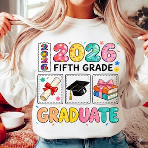 Peut inclure: Sweat-shirt blanc avec un motif graphique coloré. Le motif comprend l'année "2026", les mots "FIFTH GRADE" et "GRADUATE", ainsi que des illustrations d'un diplôme, d'une toque et de livres. Le motif est orné de fleurs et de confettis.