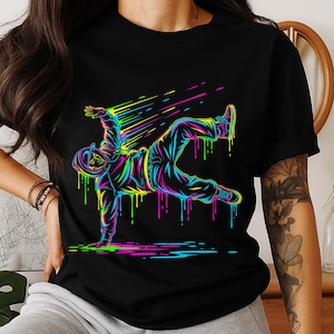 May include: Black t-shirt featuring a neon-colored illustration of a breakdancer in motion. The design includes vibrant streaks of yellow, pink, blue, and green, creating a dynamic and energetic visual. The breakdancer is depicted in a stylized, graffiti-inspired aesthetic.