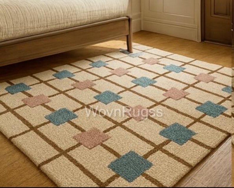 May include: Beige area rug with a brown grid pattern and alternating blue and pink diamond shapes. The rug is placed on a hardwood floor, partially under a wooden bed frame. The rug has the text "WovnRugss".