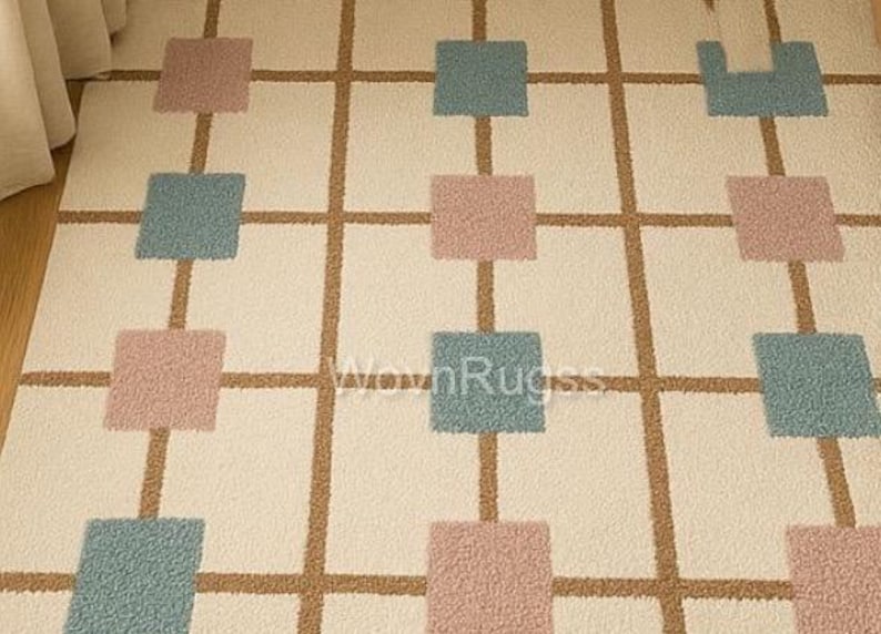 May include: A cream-colored rug with a grid pattern. The grid lines are brown, and the squares are alternating colors of dusty rose and teal. The rug has a soft, textured appearance, suitable for a living room or bedroom.