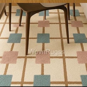 May include: A cream-colored rug with a geometric pattern of brown lines and squares in dusty rose and teal. The rug is under the legs of wooden furniture. The text "WovnRugs" is visible on the rug.