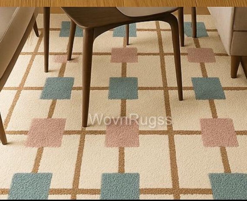 May include: A cream-colored rug with a geometric pattern of brown lines and squares in dusty rose and teal. The rug is under the legs of wooden furniture. The text "WovnRugs" is visible on the rug.