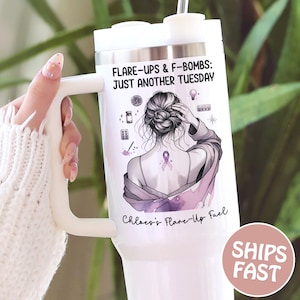 May include: White tumbler with a handle, featuring the text "FLARE-UPS & F-BOMBS: JUST ANOTHER TUESDAY" and "Chloe's Flare-Up Fuel." The design includes a woman with a purple ribbon, and small illustrations. The tumbler has a white lid and a straw.