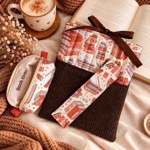 May include: A quilted book sleeve with a brown corduroy bottom and a cream top featuring a red and orange book print, tied with a brown ribbon. Includes a matching rectangular pencil case with the text "book lover" and a slim matching bookmark.