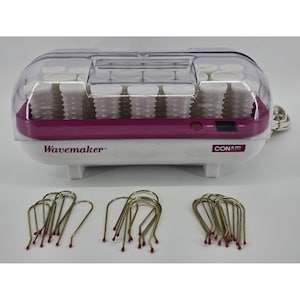 May include: A white and purple Conair Wavemaker hair curler with a clear plastic lid. The curler has multiple white rollers and gold-toned hair clips with red tips are in front.
